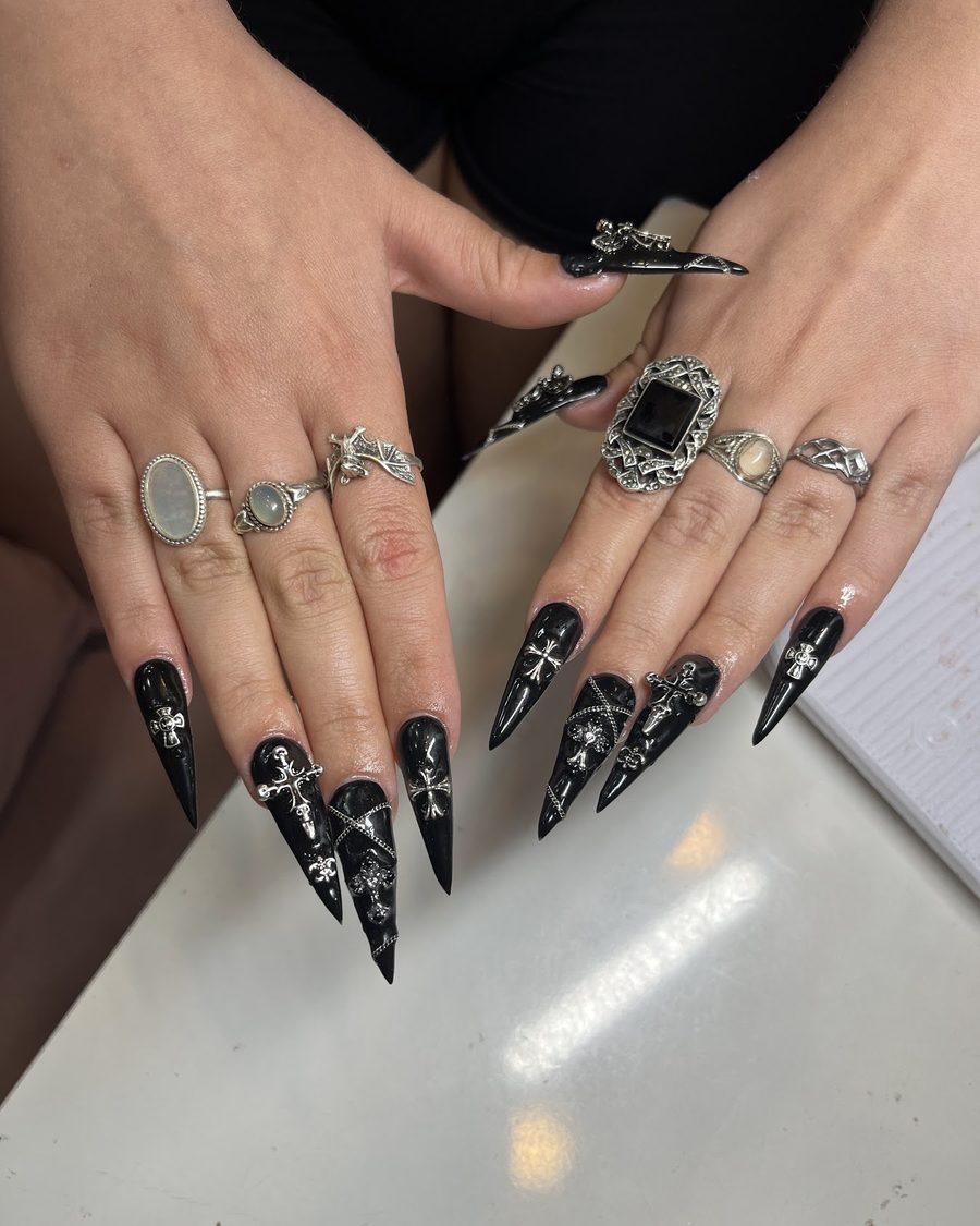 Long black stiletto nails with silver cross charms.