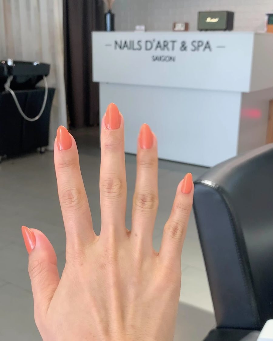 A hand resting on the desk, peach gel on short almond nails.