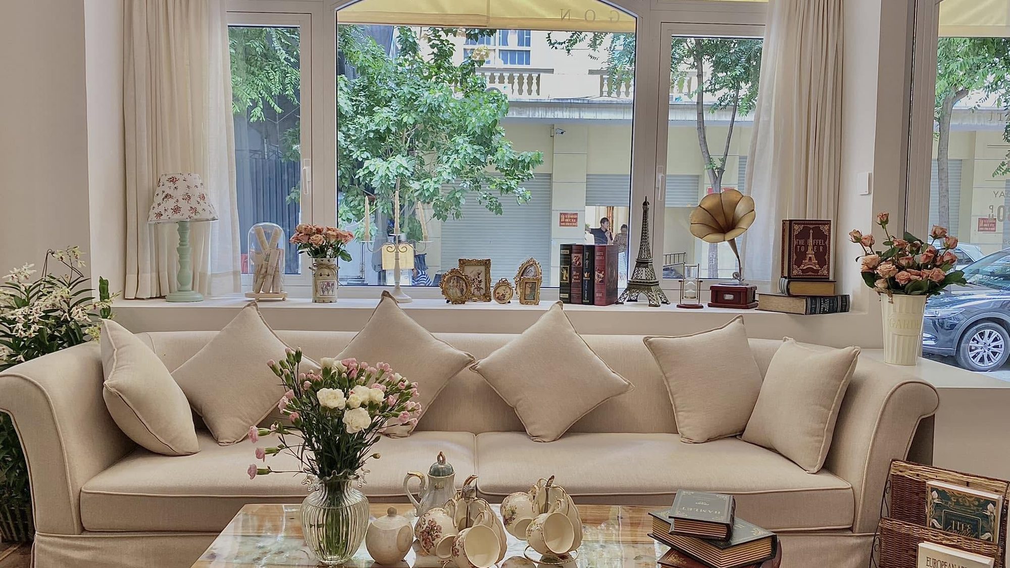 The front room, a long cream sofa and vases of roses beside the street window.