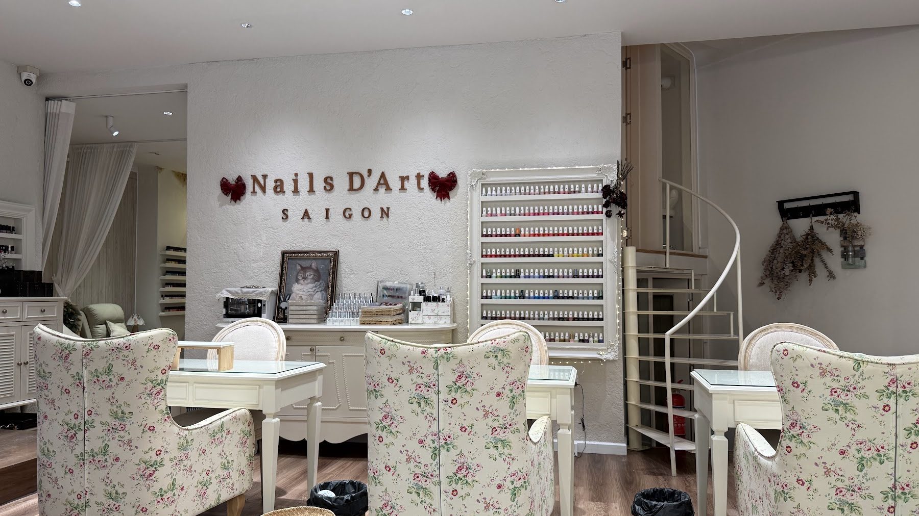 The wooden wordmark on the stucco wall between two burgundy bows, with the polish rack and the spiral stair behind.
